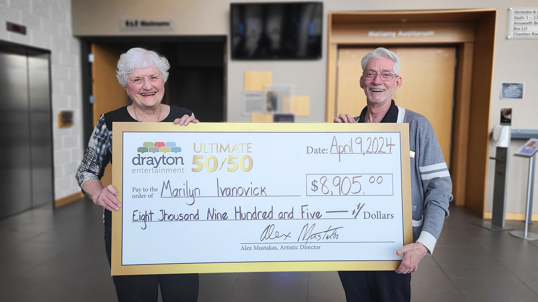 Marilyn Ivanovick and Gary Good hold a mock-up cheque in the foyer of Hamilton Family Theatre Cambridge